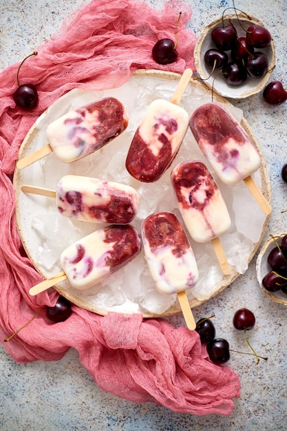 Photo fresh cream and cherry homemade popsicles placed on white ceramic plate with fruits and textile top view flat lay