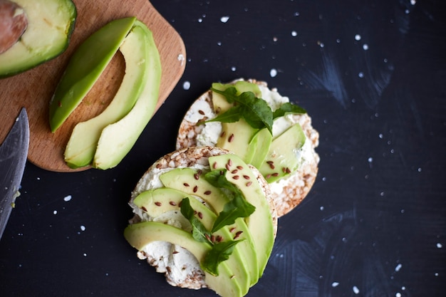 Fresh crisp bread with cream cheese, avocado and seeds on a black surface