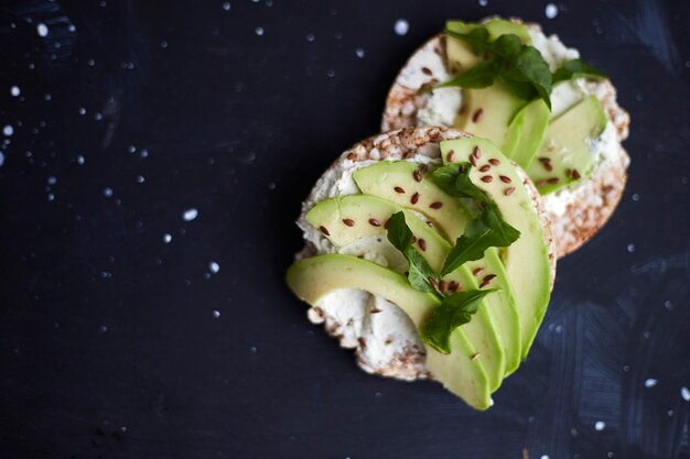 Fresh crisp bread with cream cheese, avocado and seeds on a black surface