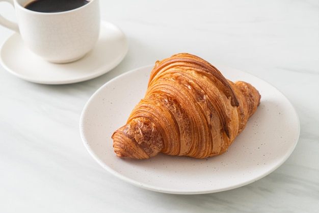 fresh croissant on white plate with black coffee