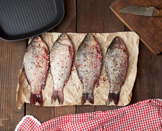 Fresh crucian fish sprinkled with spices lies on brown crumpled paper