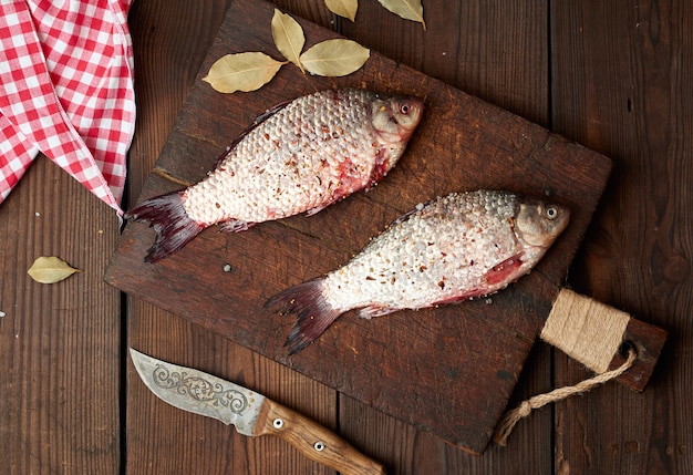 Fresh crucian fish sprinkled with spices lies on a brown wooden cutting board