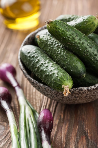 Fresh cucumbers in the bowl, green vegetables on wooden table