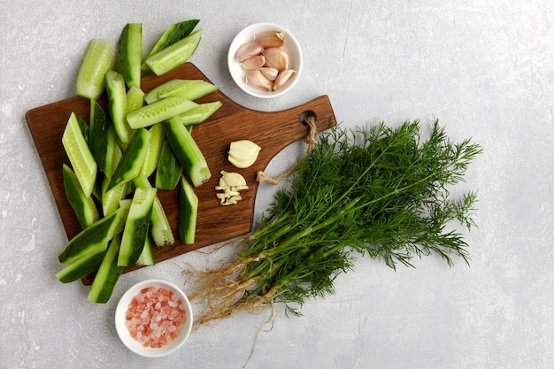 Fresh cucumbers peeled and sliced on a brown wooden cutting board with a bunch of dill garlic and pink salt