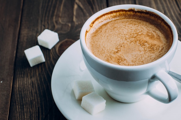 Fresh cup of coffee and sugar on old rustic table background. Morning concept