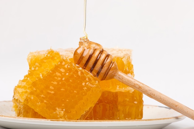 Fresh cut comb honey and wooden dipper on white