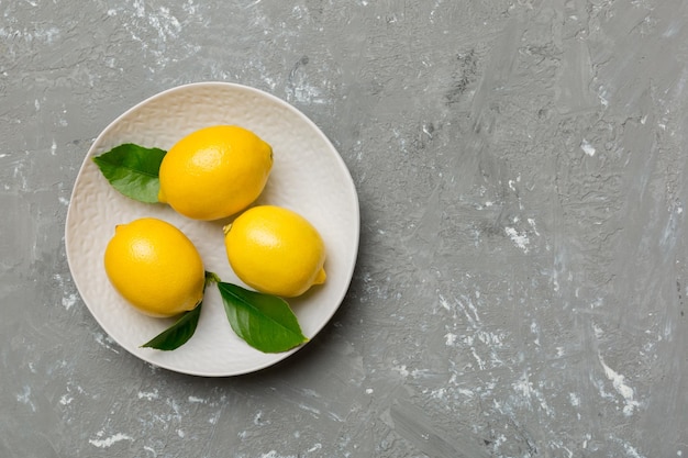 Fresh cutted lemon and whole lemons over round plate on colored background Food and drink ingredients preparing healthy eating theme top view vith copy space