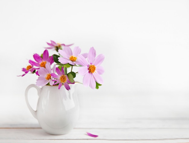 Fresh delicate pink flowers in white jar on rustic white wooden background Top view flat lay