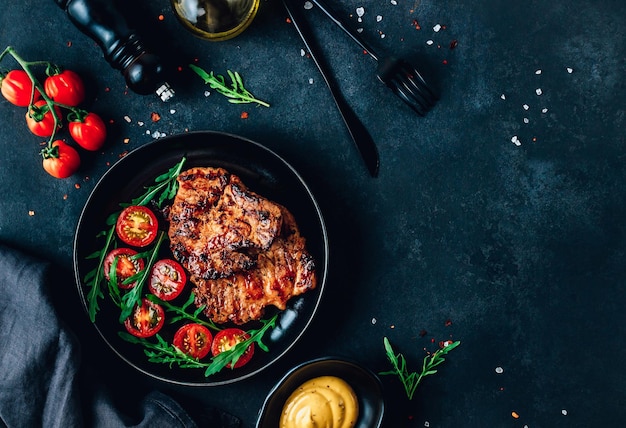 Fresh delicious juicy steaks with vegetables and spices on a dark background