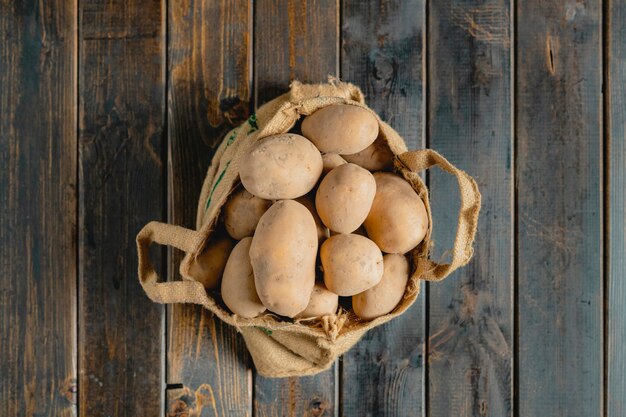 Fresh dirty potatoes in the cloth bag isolated on wooden surface b