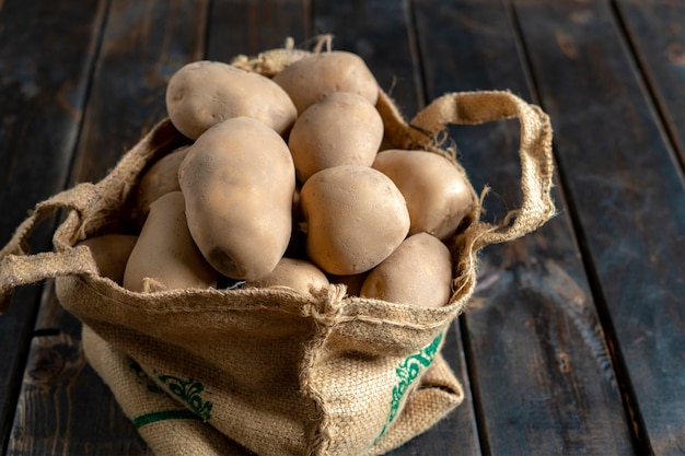 Fresh dirty potatoes in the cloth bag isolated on wooden surface b