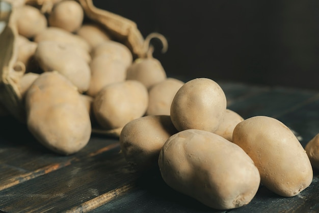 Fresh dirty potatoes in the cloth bag isolated on wooden surface b