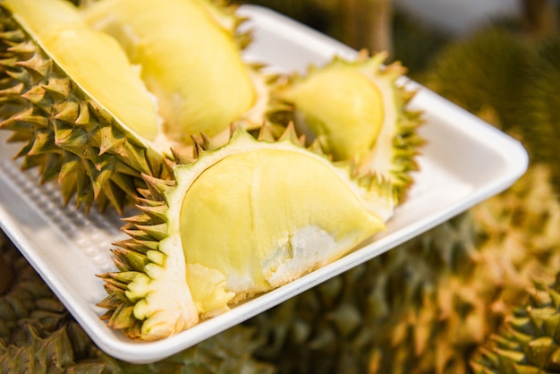 Fresh durian peeled on tray and ripe durian fruit on background for sale in the market 