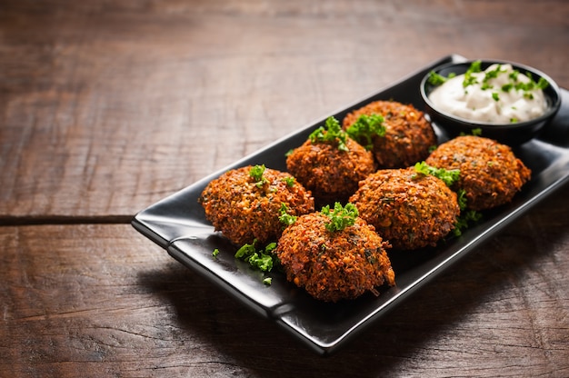 Fresh falafel with parsley and tzatziki sauce in black plate on wooden table.