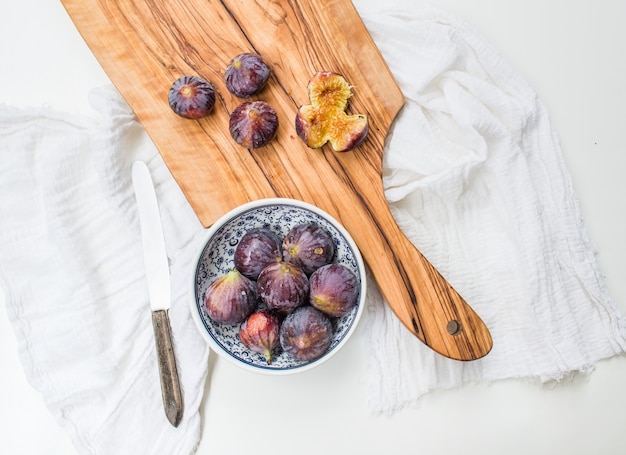 Fresh figs in blue patterned ceramic bowl and on olive wood board over white fabric