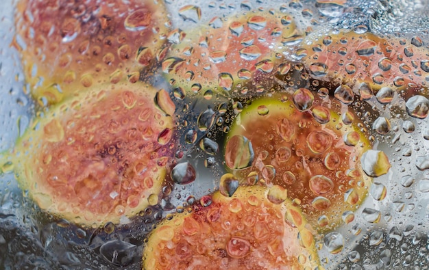 Fresh figs and fig halves on a plate under a film with drops of water Dark background closeup view from above