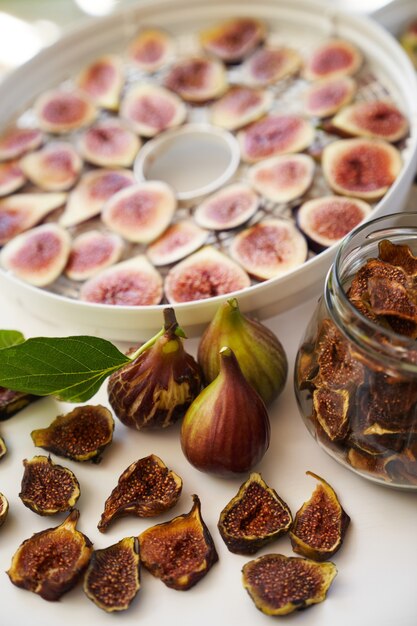 Fresh figs lie on the table next to dried figs in a glass jar and a dehydrator