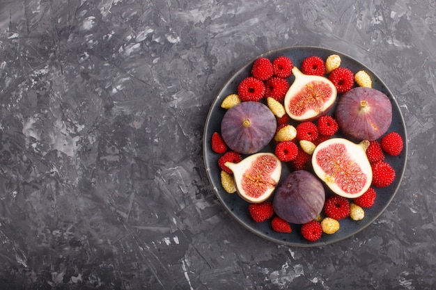 Fresh figs, strawberries and raspberries on blue plate on black concrete background