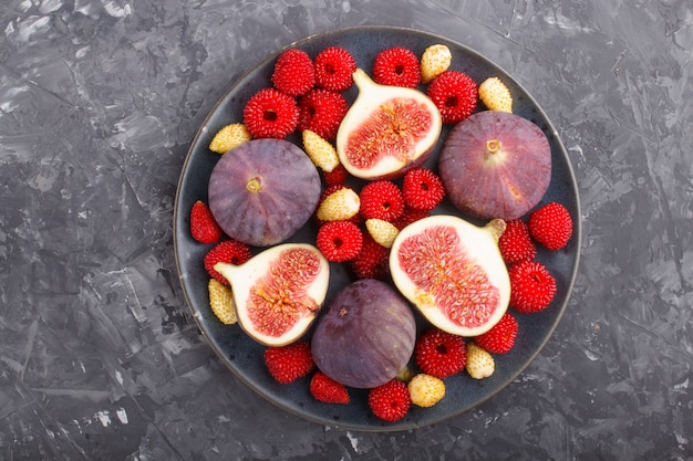 Fresh figs, strawberries and raspberries on blue plate on black concrete background