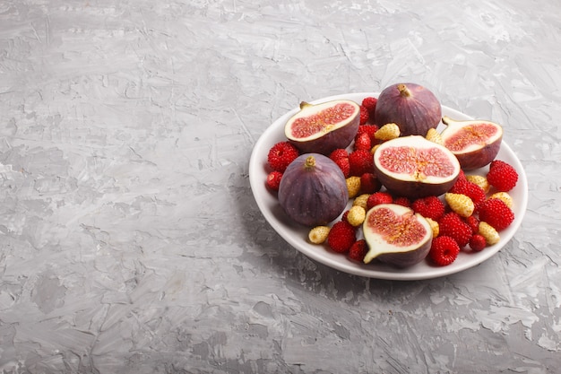 Fresh figs, strawberries and raspberries on white plate on gray concrete . side view