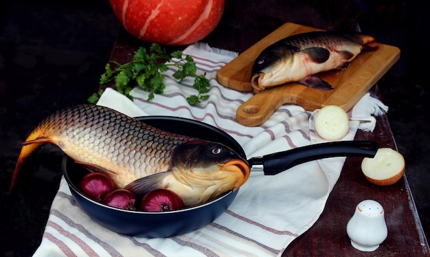 Fresh fish on a frying pan and on a cutting Board with vegetables on a dark background side viewthe concept of cooking fish dishes with vegetables