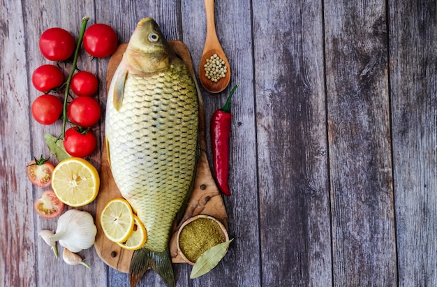 Fresh fish ready to cook background. Carp on a wooden kitchen Board in the kitchen surrounded by vegetables (pepper, garlic, cherry tomatoes, lemon).