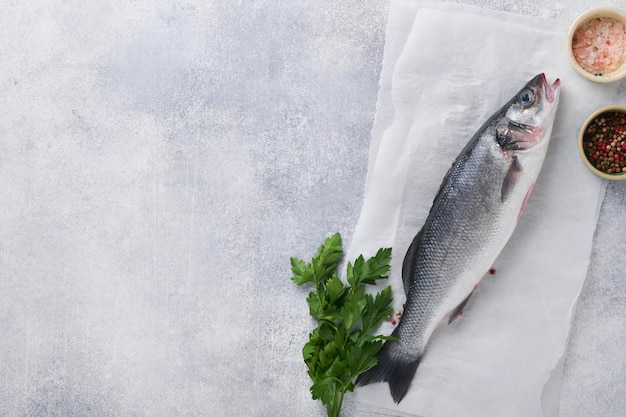 Fresh fish Sea Bass raw with salt pepper parsley olive oil and lemon on cutting board on light gray concrete rustic background Food cooking background Top view copy space