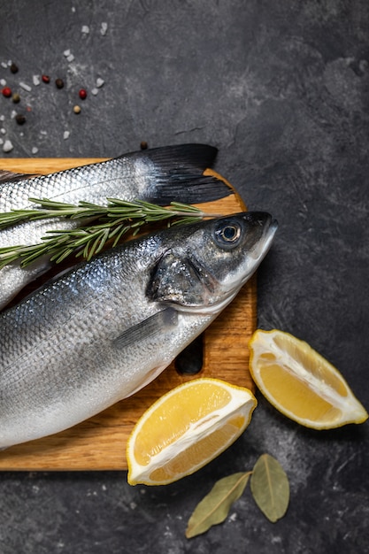 Fresh fish seabass and ingredients for cooking, lemon and rosemary. Dark background top view.