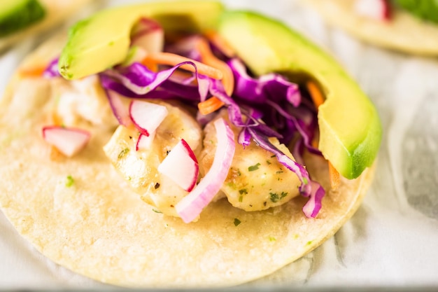 Fresh fish tacos with cod and purple cabbage on a white corn tortillas.