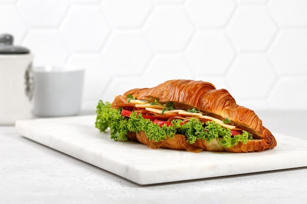 Fresh french croissant with cheese tomatoes lettuce on marble board and grey background Morning food