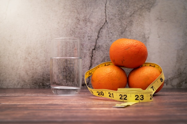 Fresh fruit for diet, measuring tape and drinking water on wooden table. Concept of diet and healthy lifestyle