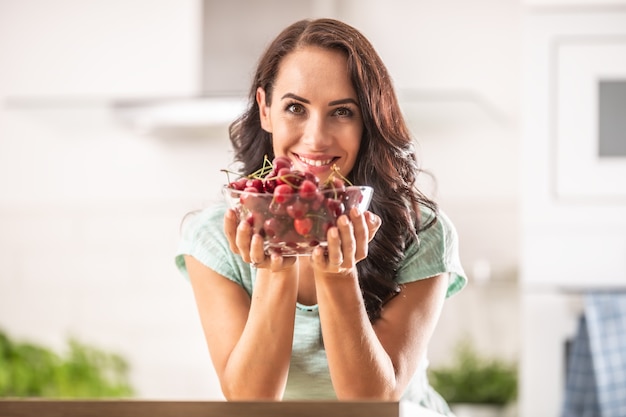 Fresh fruit harvest in the form of cherries in a seethrough bowl held by a woman indoors.