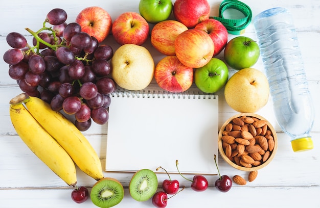 Fresh fruit and measure tape with water on white wooden background