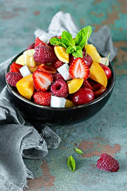 Fresh fruit salad in a black bowl on a blue background Healthy natural organic food low calories