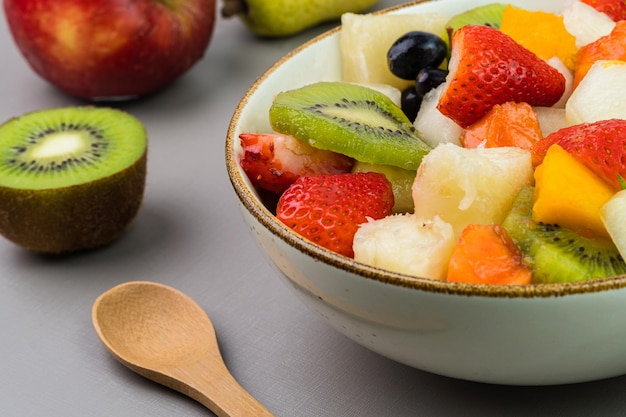 Fresh fruit salad in a bowl Multicolored and tropical fruits Pineapple mango grape strawberry papaya melon kiwi Additional with chestnuts and granola Selective focus