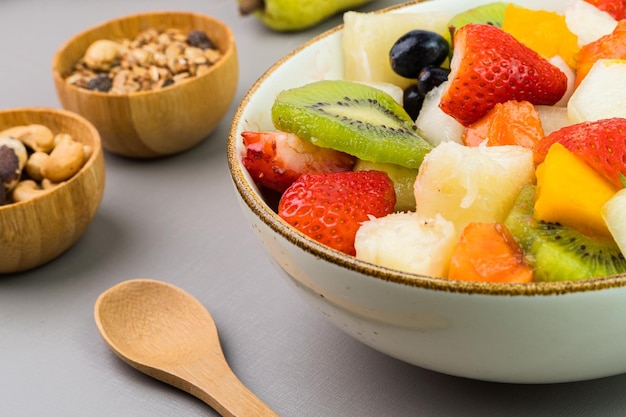 Fresh fruit salad in a bowl Multicolored and tropical fruits Pineapple mango grape strawberry papaya melon kiwi Additional with chestnuts and granola Selective focus