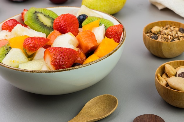 Fresh fruit salad in a bowl Multicolored and tropical fruits Pineapple mango grape strawberry papaya melon kiwi Additional with chestnuts and granola Selective focus