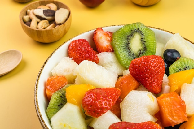 Fresh fruit salad in a bowl Multicolored and tropical fruits Pineapple mango grape strawberry papaya melon kiwi Additional with chestnuts and granola Selective focus