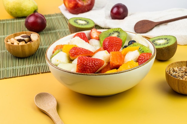 Fresh fruit salad in a bowl Multicolored and tropical fruits Pineapple mango grape strawberry papaya melon kiwi Additional with chestnuts and granola Selective focus