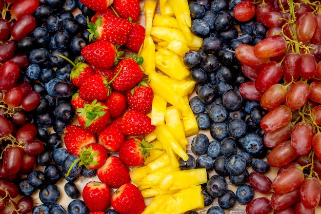 Fresh fruits background Arrangement in row of grapes assorted berries and slice pineapple