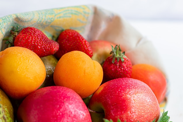 Fresh fruits in an eco cotton bag on a table in the kitchen. with apples and pears, apricots and strawberries, zero waste trading concept. Ban plastic.