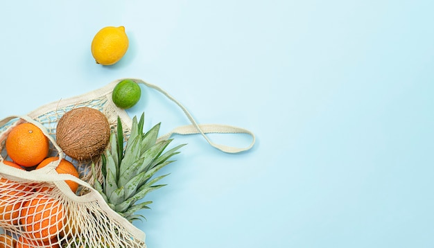 Fresh fruits in a mesh bag on a light blue background