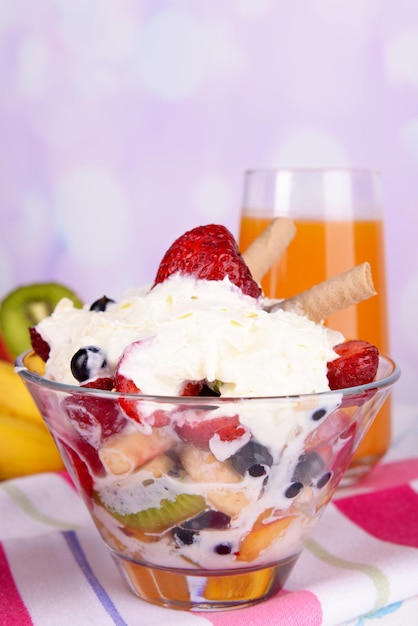 Fresh fruits salad with ice cream in bowl and juice on bright background