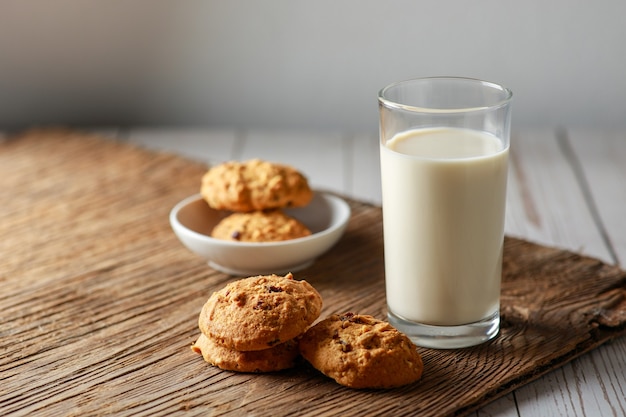 A fresh glass of milk with chocolate chip cookies on white wooden surface