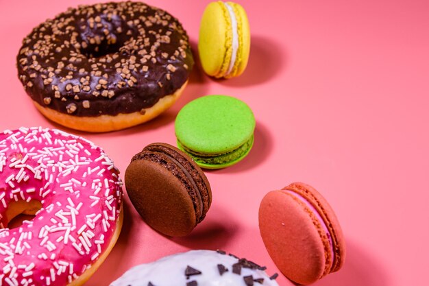 Fresh glazed donuts and french macaroons isolated on a pink background