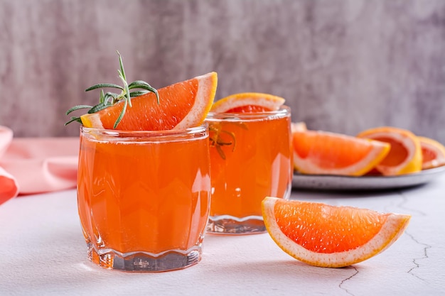 Fresh grapefruit juice with rosemary and pieces of fruit in glasses on the table