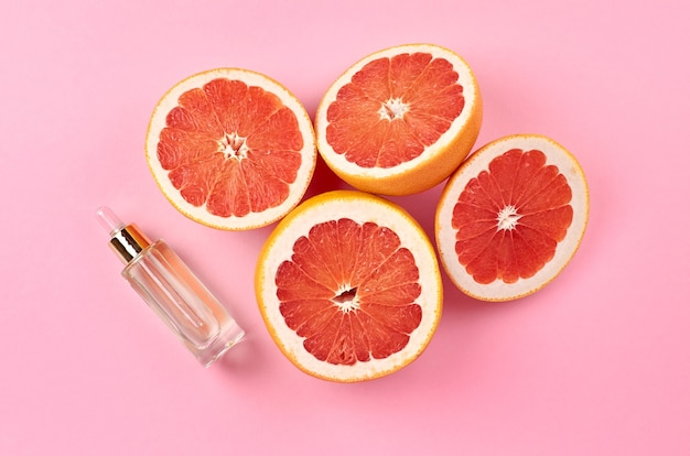 Fresh grapefruit slices with oil glass bottle on pink background