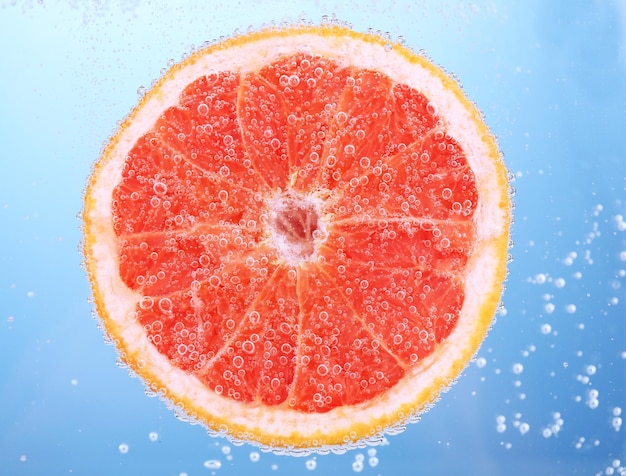 Fresh grapefruit in water with bubbles on blue background