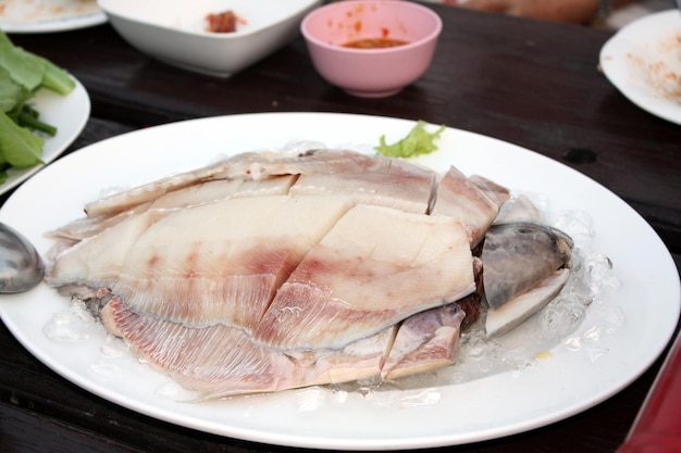 Fresh Gray pomfret Chinese silver pomfret fish cut into pieces arranged in a white plate topped with ice On the wooden table in the restaurant prepare for the shabu pot Selective focus