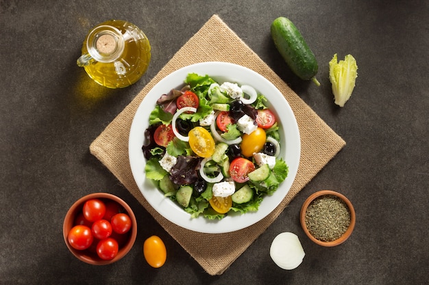 Fresh greek salad in plate and ingredients on stone table